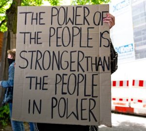 Person holding sign that says power of the people is stronger thn the people in power