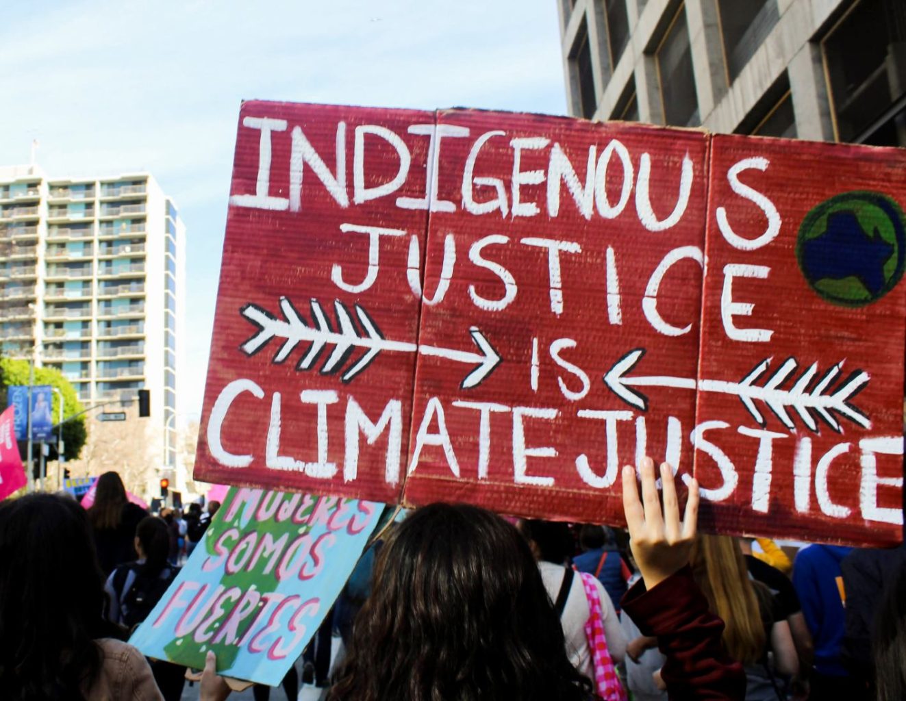 A poster reading Indigenous Justice Is Climate Justice is held high at a rally 
